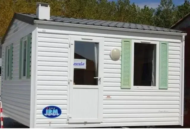 Mobil-home blanc aux volets vert pâle installé dans un environnement arboré