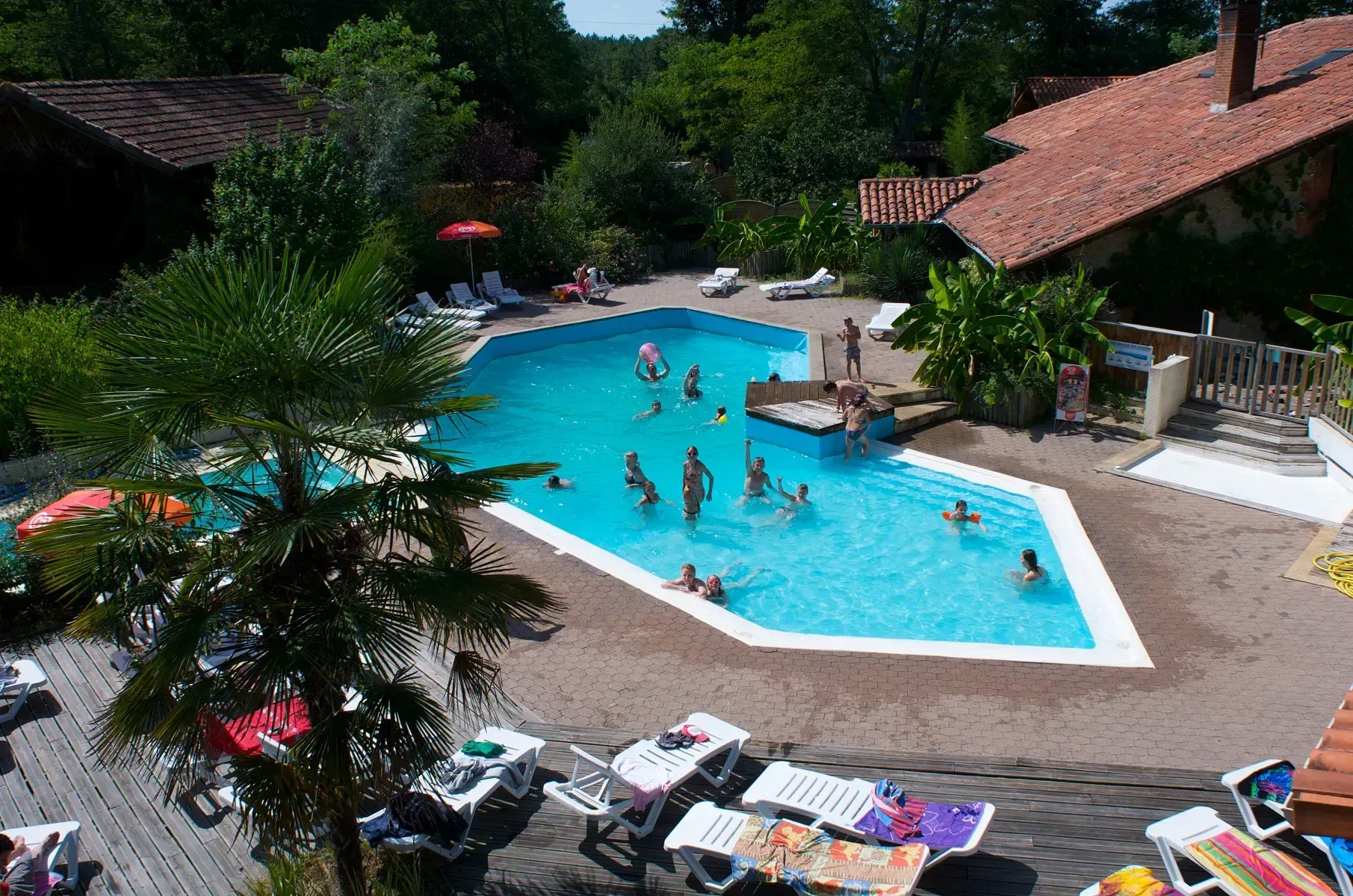 Vue en hauteur de la piscine du camping à Saint-Justin avec des familles dans l'eau et des transats autour du bassin