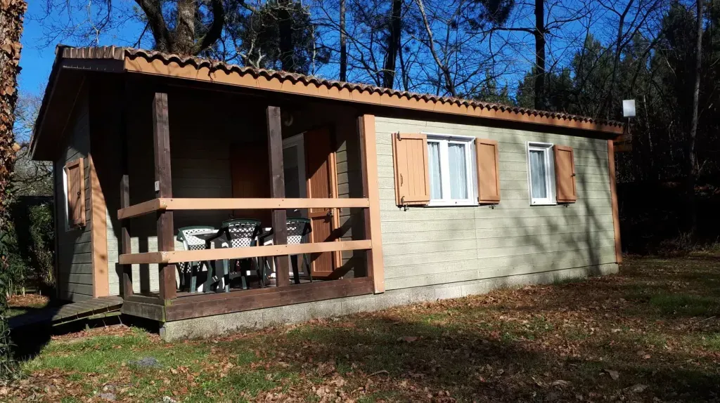 Chalet beige avec volets en bois et terrasse couverte sur un terrain arboré