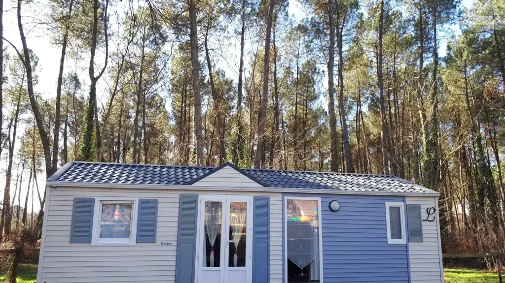 Grand mobil-home blanc et bleu entouré de hauts pins