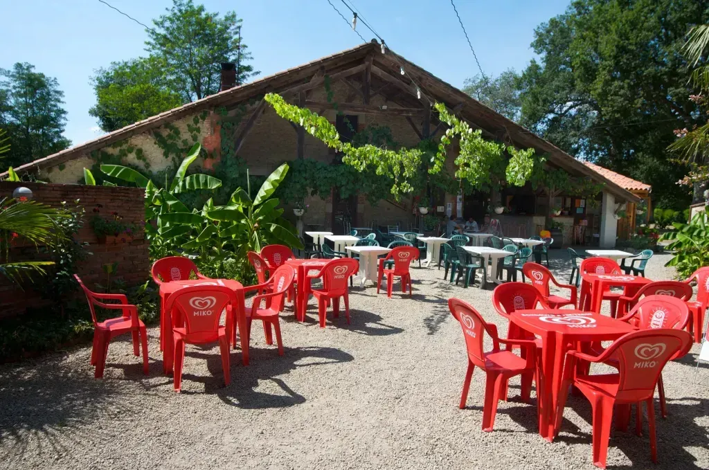 Terrasse extérieure du restaurant avec tables et chaises devant un bâtiment couvert de végétation