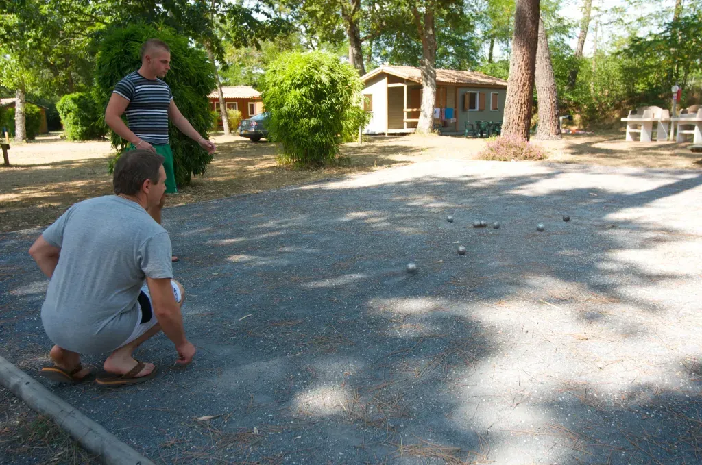 Deux campeurs jouant à la pétanque sur un terrain ombragé près des chalets