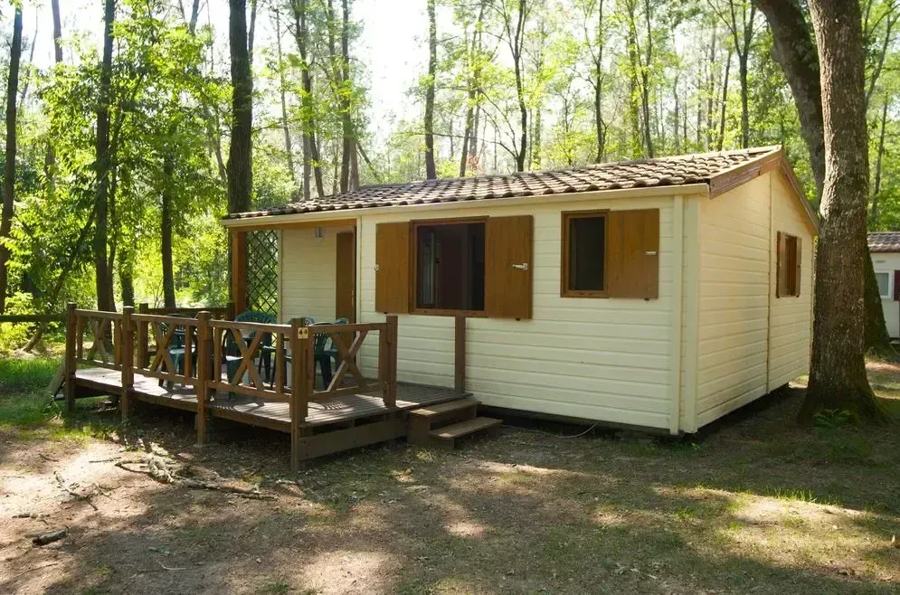 Chalet clair avec volets et terrasse en bois sur un emplacement ombragé