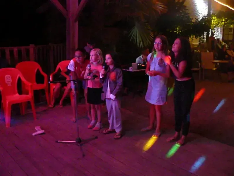 Enfants et adultes chantant au micro lors d'une animation karaoké en soirée au camping