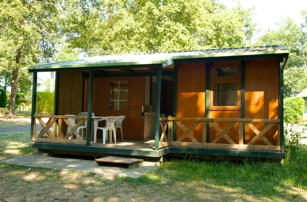 Bungalow en bois brun avec terrasse couverte et chaises blanches dans un cadre arboré