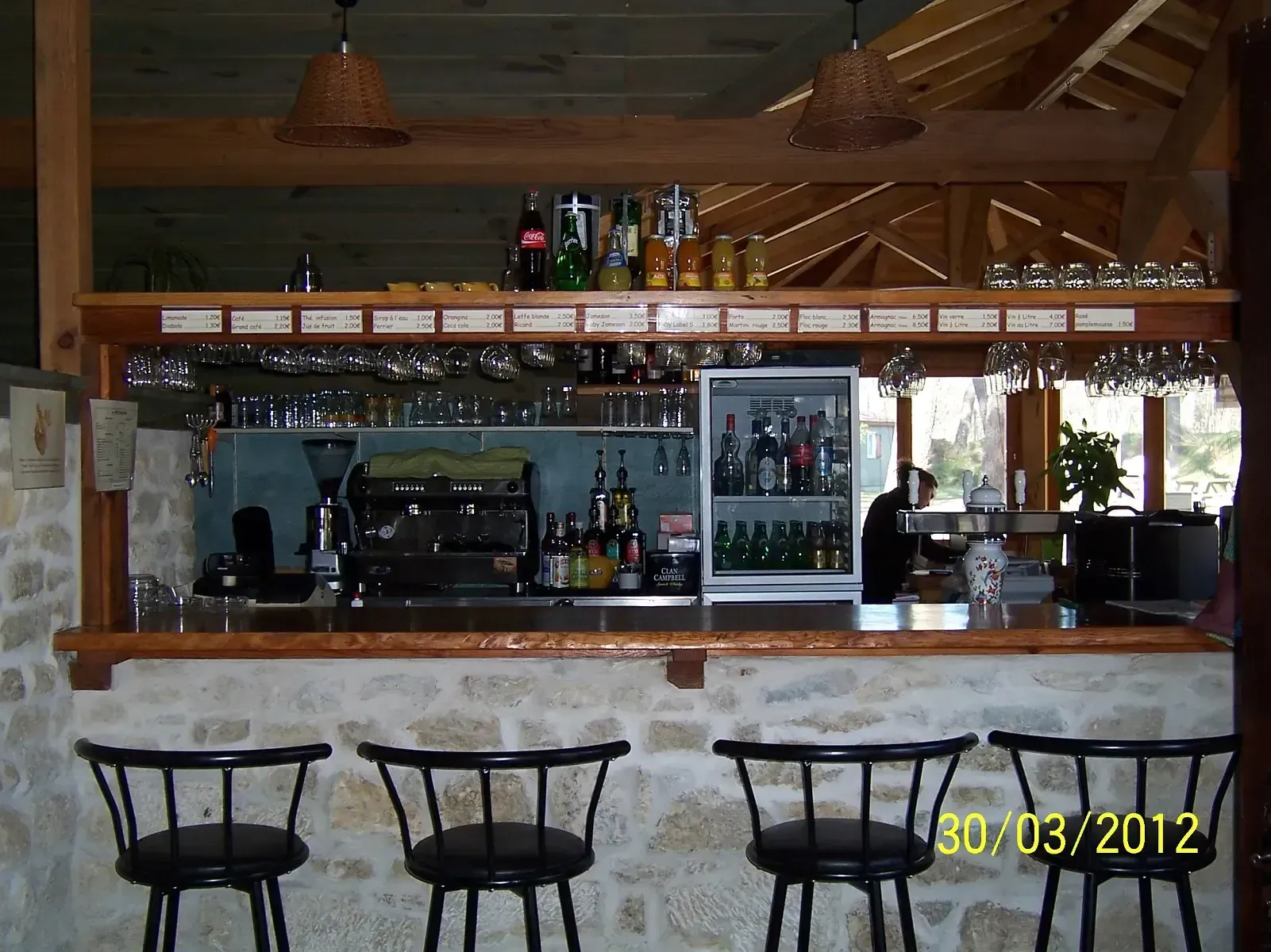 Comptoir en pierre et en bois du bar du camping, avec machine à café, boissons et tabourets
