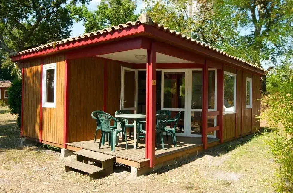 Chalet en bois brun et rouge avec terrasse couverte et salon de jardin vert