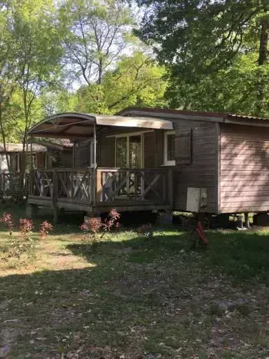 Mobil-home brun avec terrasse couverte en bois sur un emplacement ombragé