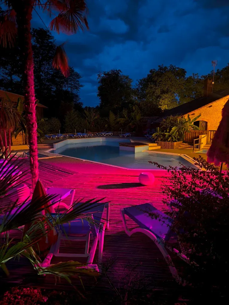 Piscine extérieure avec baigneurs au milieu des arbres et des bâtiments du camping