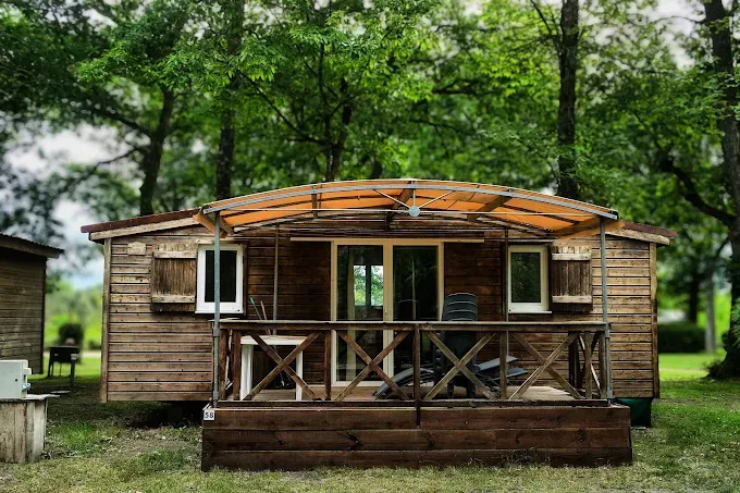 Mobil-home en bois avec terrasse et auvent orange sous de grands arbres