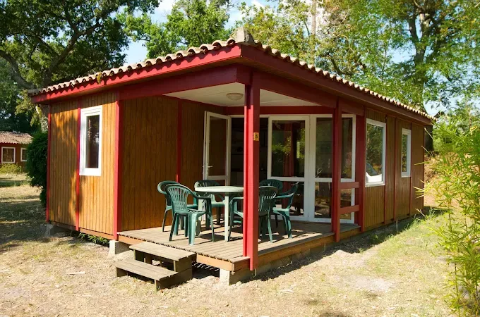 Chalet en bois avec terrasse couverte et mobilier de jardin dans un cadre arboré